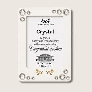 Puede incluir: Un marco de fotos rectangular blanco decorado con cristales transparentes en las esquinas. El inserto central presenta el texto 15th Anniversary, Crystal, Signifies clarity and transparency within a relationship, Congratulations from y Front Porch Homes.