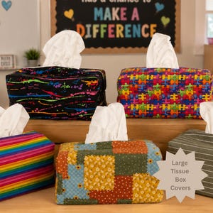 May include: Five rectangular fabric tissue box covers featuring various patterns including a black cover with neon paint splatters, a colorful jigsaw puzzle print, a rainbow striped design, a floral patchwork print, and a dark green striped cover.