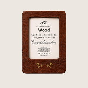 Puede incluir: Un marco rectangular de madera marrón oscuro que contiene una tarjeta blanca con el texto 5th ANNIVERSARY Wood Signifies deep roots and a solid, stable foundation Congratulations from FRONT PORCH HOMES y un dibujo lineal de una casa.