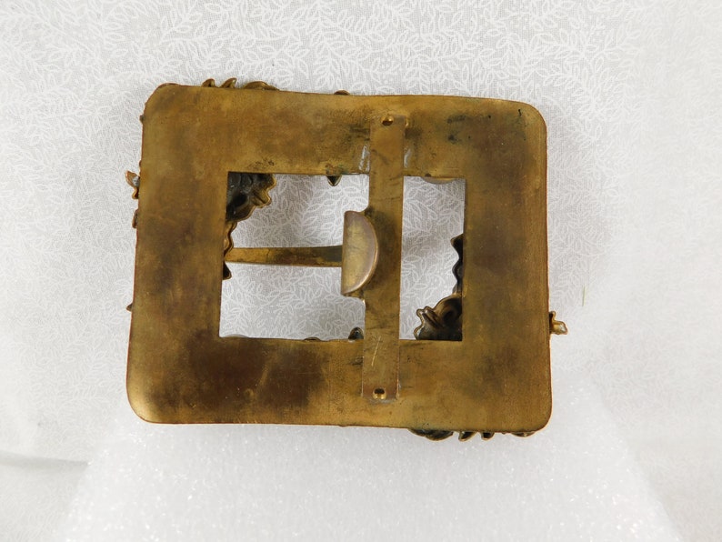 K&ouml;nnte beinhalten: Eine goldfarbene G&uuml;rtelschnalle mit einem verzierten Design. Die Schnalle hat eine rechteckige Form mit einer kleineren rechteckigen &Ouml;ffnung in der Mitte. Die Schnalle ist mit komplizierten Blumenmustern verziert.