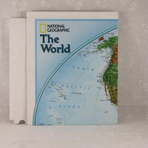 May include: A hardcover book titled "The World" by National Geographic. The cover features a world map with blue oceans and green and brown landmasses. The title is in large, blue letters.