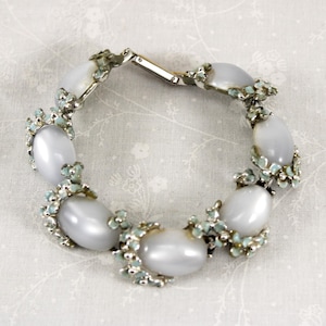 May include: A vintage bracelet featuring oval, pearlescent gray stones set in a silver-tone metal. The bracelet has a floral design with small, light blue accents. The clasp is a simple, secure design.