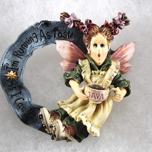 May include: A whimsical figurine of a fairy holding a coffee cup labeled "JAVA." The fairy is dressed in a green and cream-colored outfit with pink wings. A blue ring behind the fairy reads "I'm Running As Fast As I Can!!!"