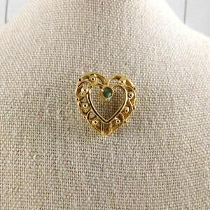May include: A gold heart-shaped brooch with a green gemstone in the centre.