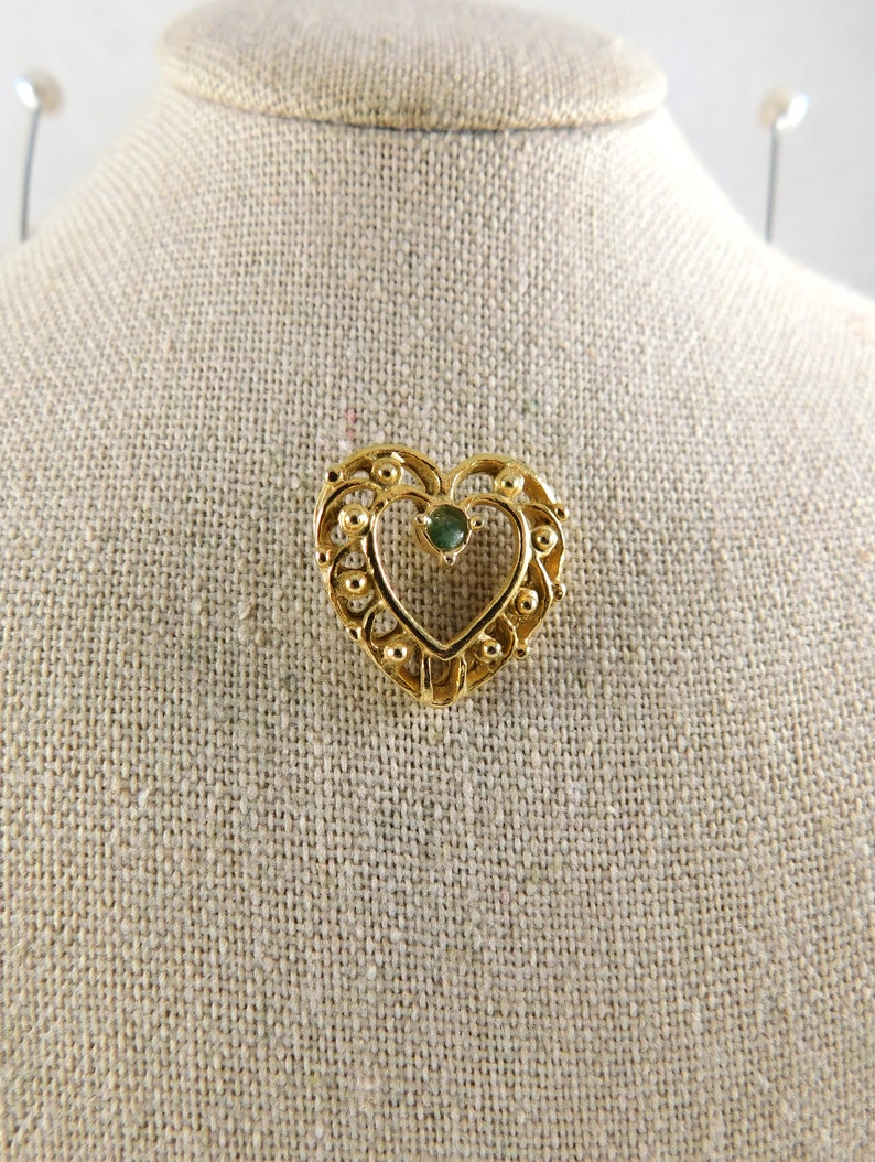 May include: A gold heart-shaped brooch with a green gemstone in the centre.