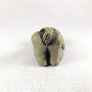 May include: A small, grey, ceramic sculpture of a person sitting with their head down and their arms wrapped around their legs.