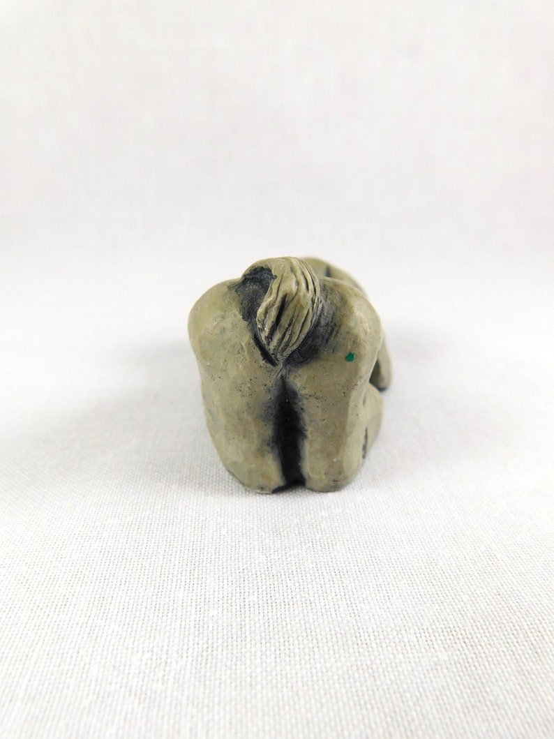 May include: A small, grey, ceramic sculpture of a person sitting with their head down and their arms wrapped around their legs.
