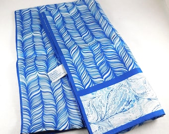 May include: A blue silk scarf with a white abstract pattern. The scarf is folded in half and has a blue border. The label reads "Hand-painted Exclusively for The Gallery, Inc. Made in Italy."