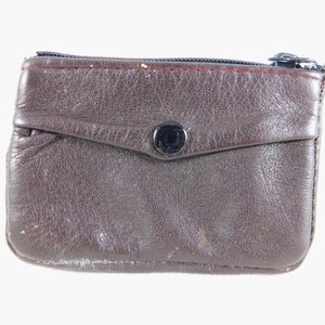May include: A brown leather coin purse with a zipper closure and a snap button. The purse has a small pocket on the front.