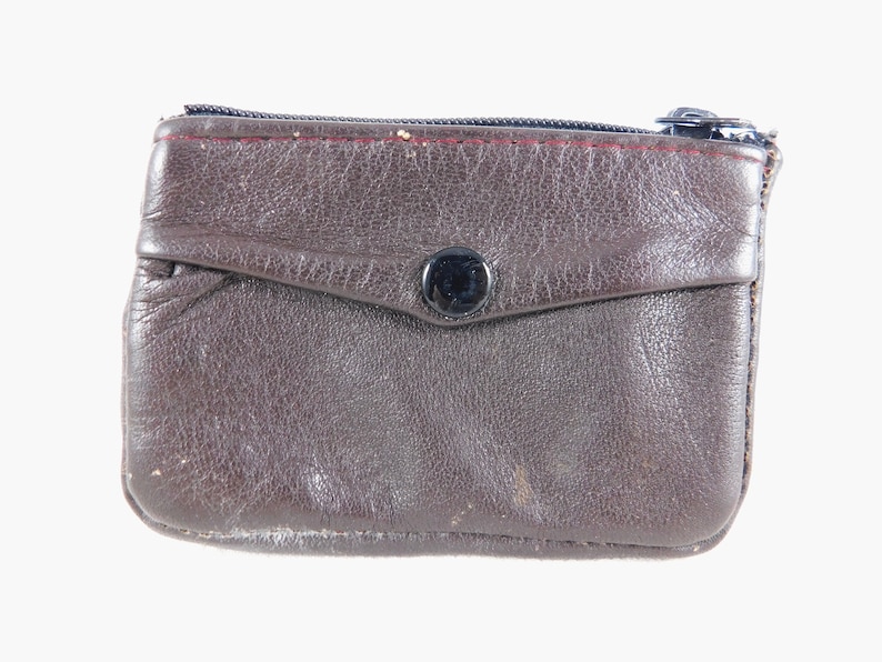 May include: A brown leather coin purse with a zipper closure and a snap button. The purse has a small pocket on the front.