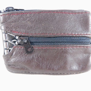 May include: A brown leather coin purse with a zipper closure. The purse has a red stitch detail around the edges.