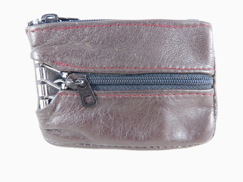 May include: A brown leather coin purse with a zipper closure. The purse has a red stitch detail around the edges.