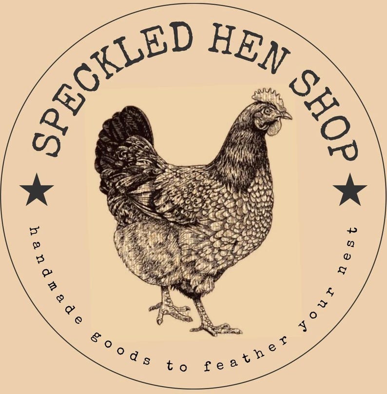 Op de afbeelding: Een bruine gevlekte hen met een witte ster aan elke kant van de cirkel. De tekst "Speckled Hen Shop" staat in een cirkel rond de hen. De tekst "handmade goods to feather your nest" staat in een cirkel rond de hen.