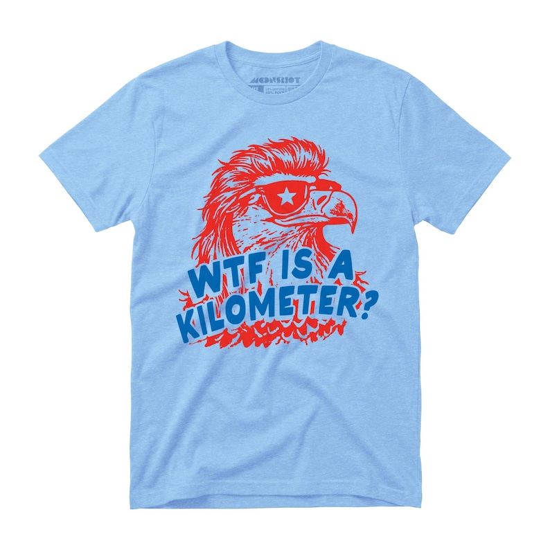 May include: Light blue t-shirt featuring a red eagle wearing sunglasses with a star and the text "WTF IS A KILOMETER?" in blue. The eagle graphic has a retro design. The shirt is made of a soft material.