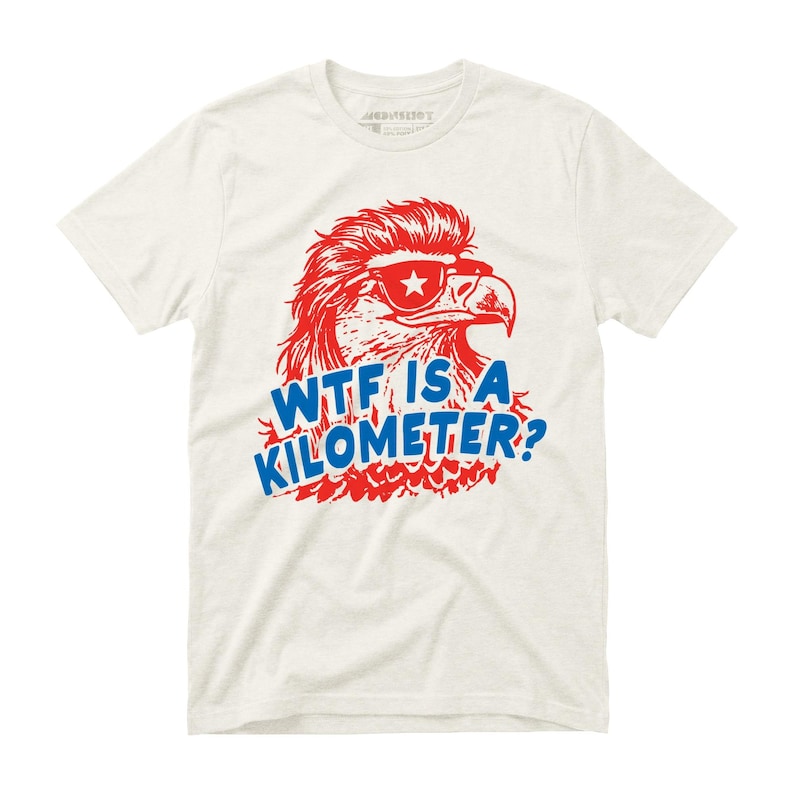 May include: Off-white t-shirt featuring a red and blue graphic of an eagle wearing sunglasses with a star. The text "WTF IS A KILOMETER?" is in blue. The shirt has a crew neck and short sleeves.