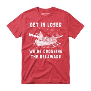 May include: Red t-shirt with a white graphic of a boat crossing a river, featuring a historical scene with the text "GET IN LOSER WE'RE CROSSING THE DELAWARE". The shirt has a crew neck and short sleeves.