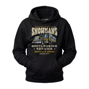May include: Black hooded sweatshirt with a graphic featuring a semi-truck and the text "SNOWMAN'S BOOTLEGGING SERVICE Texarkana to Atlanta SINCE 1977". The design includes the phrase "East Bound & Down, Loaded Up & Truckin".