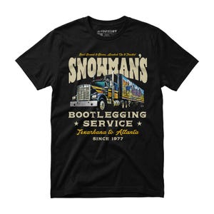 May include: Black t-shirt featuring a graphic of a semi-truck with the text "SNOWMAN'S BOOTLEGGING SERVICE Texarkana to Atlanta SINCE 1977". The truck has a colorful mural on the trailer.