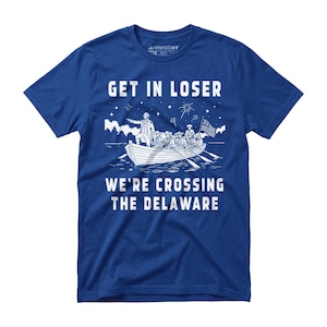 May include: Blue t-shirt with white graphic of a boat crossing water, with text "GET IN LOSER" above and "WE'RE CROSSING THE DELAWARE" below. The boat has people and an American flag.