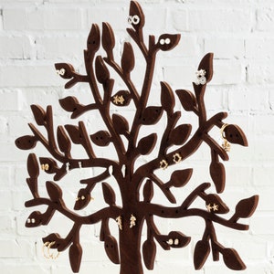 The dark brown tree of the jewelry holder is made of wood. Earrings hang from a laser-cut tree. A close-up of part of a jewelry  tree.