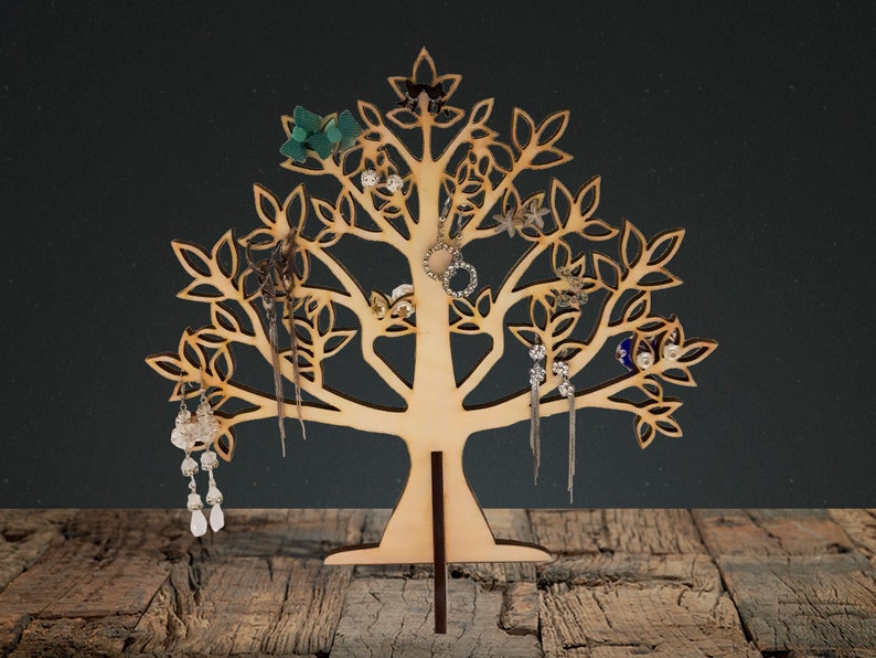 The light brown tree of the jewelry holder is made of wood. Earrings hang from a laser-cut tree.