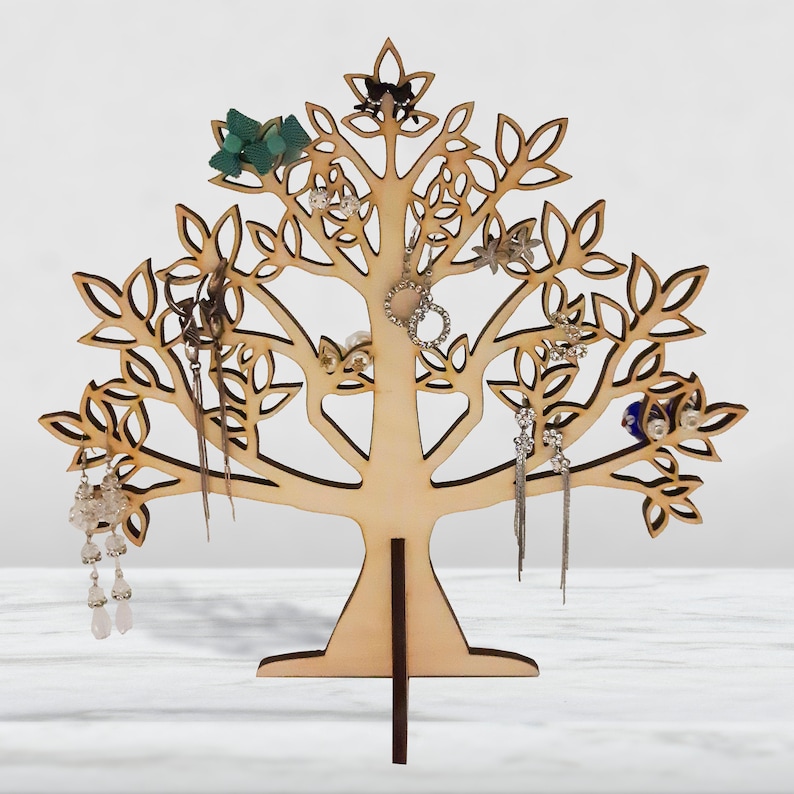 The light brown tree of the jewelry holder is made of wood. Earrings hang from a laser-cut tree.