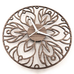 Op de afbeelding: Een bruine houten wandklok met een wit ingewikkeld ontwerp en witte wijzers. De klok is rond en heeft een diameter van ongeveer 30 cm.