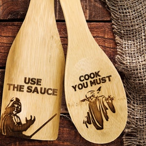 Wooden spatula and spoon set. Wooden spoon on the right. The spoon is engraved with Baby Yoda and the inscription - cook you must. Spatula on the left. The spatula is engraved with Darth Vader and the inscription - Use the sauce.