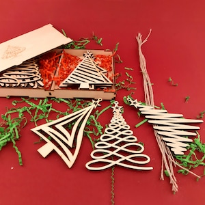 3 laser-cut Christmas trees are removed from the wooden box with Christmas trees. The wooden box is engraved with Merry Christmas and a Christmas tree.  Linen ropes are placed next to the Christmas trees.