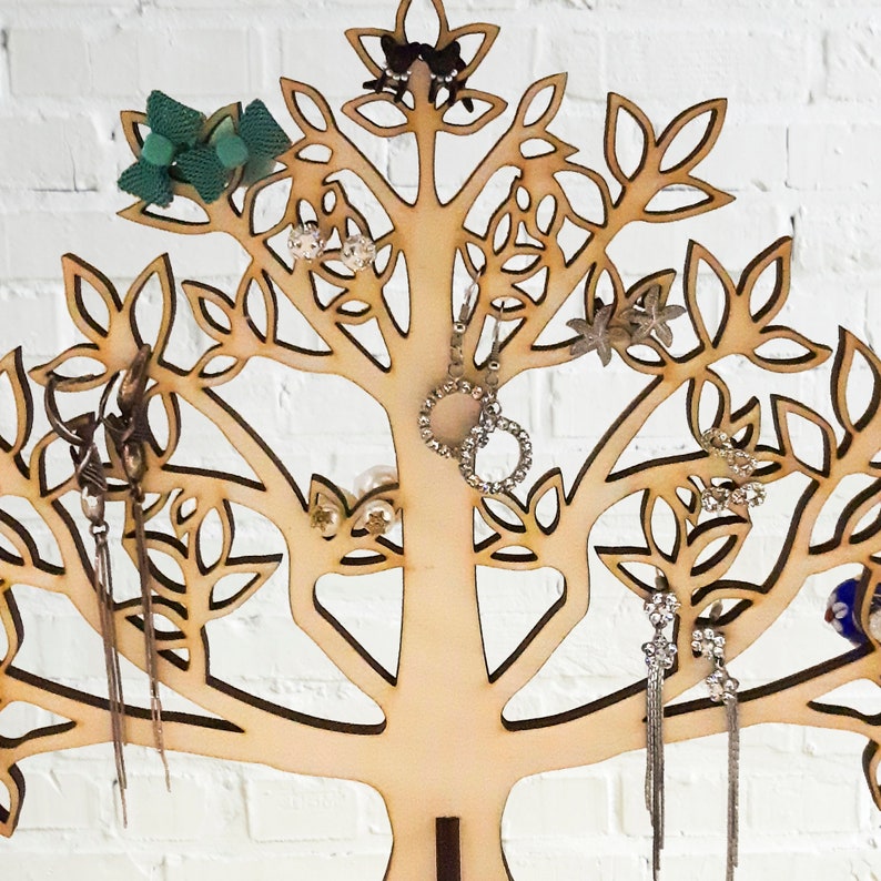 A close-up of part of a jewelry tree. The light tree of the jewelry holder is made of wood. Earrings hang from a laser-cut tree.