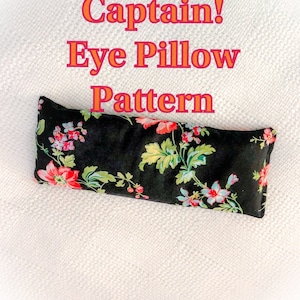 Può includere: Un cuscino per gli occhi nero con una stampa floreale in tonalità di rosso, rosa, blu e verde. Il cuscino è su una superficie bianca testurizzata. Il testo "Eye-Eye Captain! Eye Pillow Pattern" è scritto in arancione sopra il cuscino.