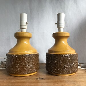 May include: A pair of ceramic table lamps with a textured brown and yellow glaze. The lamps have a simple, mid-century modern design.