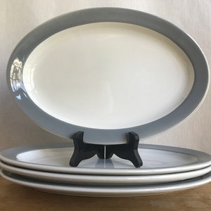May include: A set of four oval ceramic plates with a grey rim and white centre. The plates are stacked on top of each other.