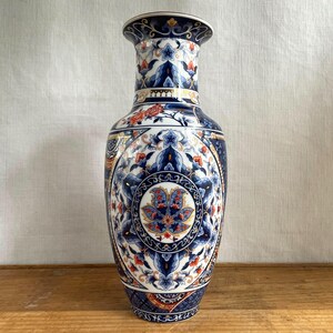 May include: A tall, decorative ceramic vase with a detailed floral pattern in shades of blue, white, and orange. The vase features a flared top and a rounded body, with intricate designs encircling the surface. The vase is approximately 30 cm tall.