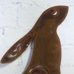 May include: A weathered, rusty brown metal hare garden ornament. The hare features decorative cut-out details on the ear and body, and a crescent moon shape on the head. It is mounted on two metal stakes for garden display.