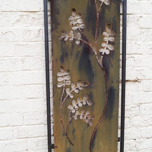 May include: A metal garden screen with a rusted finish and a cut-out design of stylised plants. The screen is framed in black metal.