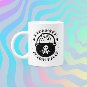 May include: White ceramic mug with a black and white graphic of a cauldron with flames and a skull and crossbones. The text "Licensed Potion Maker" is around the cauldron.