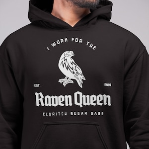 May include: Black hooded sweatshirt with a white graphic design featuring a raven, the text "I work for the Raven Queen", "Est. 2020", and "Eldritch Sugar Babe".