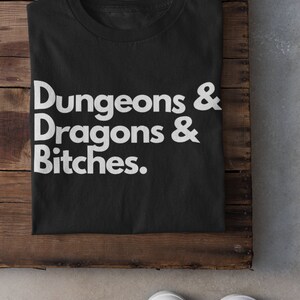 May include: Black t-shirt with white text that reads "Dungeons & Dragons & Bitches."