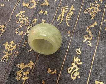 May include: A light green jade ring with a smooth, polished surface. The ring is round and has a hole in the centre. The ring is sitting on a dark brown surface with gold Chinese characters.