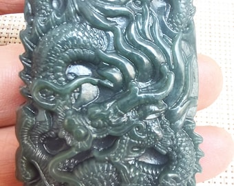 Op de afbeelding: Een donkergroene jade hanger gegraveerd met een gedetailleerd drakenontwerp. De draak is afgebeeld in een opgerolde positie met zijn kop omhoog en zijn staart om zijn lichaam gekruld. De hanger heeft een glad, gepolijst oppervlak.