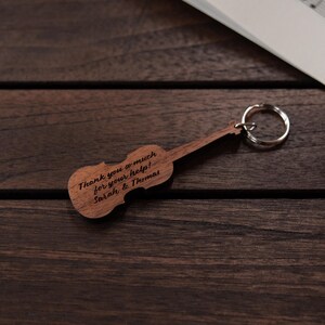 Puede incluir: Llavero de viol&iacute;n de madera con un mensaje personalizado: "&iexcl;Muchas gracias por tu ayuda! Sarah & Thomas".