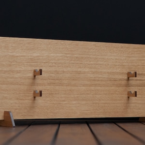 May include: A wooden wall-mounted display stand with four hooks for hanging items. The stand has a light brown finish and is made of wood.