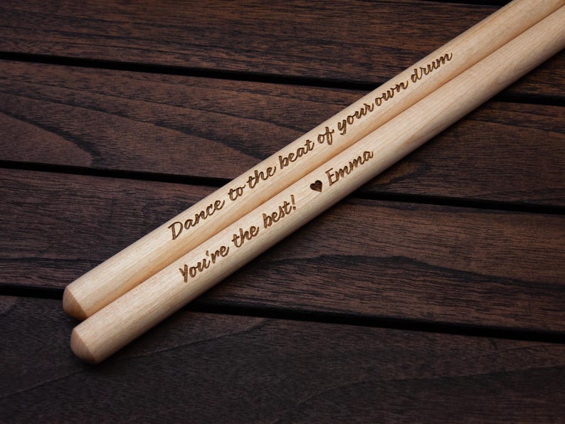 May include: A pair of wooden drumsticks with the text "Dance to the beat of your own drum" and "You're the best!"  The second drumstick also has a heart symbol and the name "Emma" engraved on it.