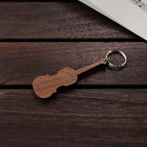 Puede incluir: Un llavero de madera con forma de viol&iacute;n con un anillo de llave plateado. El llavero est&aacute; sobre una superficie de madera marr&oacute;n oscura.