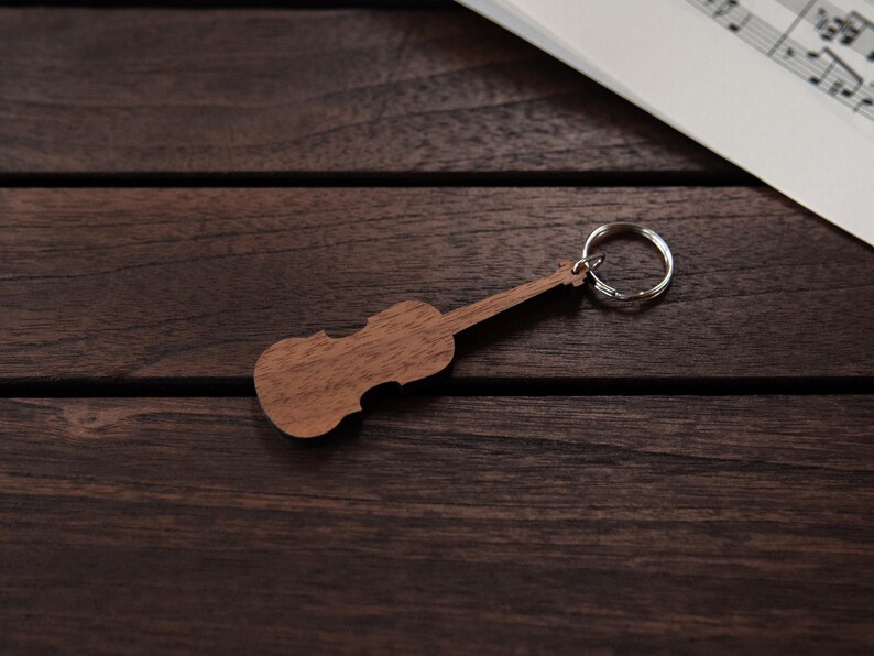 Puede incluir: Un llavero de madera con forma de viol&iacute;n con un anillo de llave plateado. El llavero est&aacute; sobre una superficie de madera marr&oacute;n oscura.
