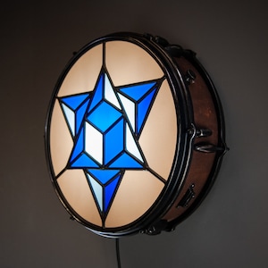 May include: A blue and white stained glass star design inside a round drum with a brown wooden surface and black metal hardware.