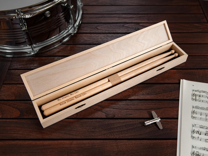May include: A wooden box with a hinged lid, containing two wooden drumsticks. The drumsticks are engraved with the text "No Drum, No Life" and "Know Drum, Know Life".
