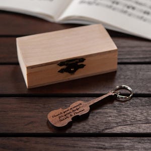 Puede incluir: Un llavero de viol&iacute;n de madera con la inscripci&oacute;n "Thank you so much for your help! Sarah & Thomas" sobre un fondo de madera con una peque&ntilde;a caja de madera.