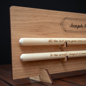May include: A wooden plaque with a personalized message for Joseph M. Williams. The plaque has two wooden dowels with engraved messages: "All the best from your dear colleagues" and "To the world's okayest drummer".